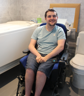 Tim Hayes in a wheelchair accessible bathroom next to his assistive bath